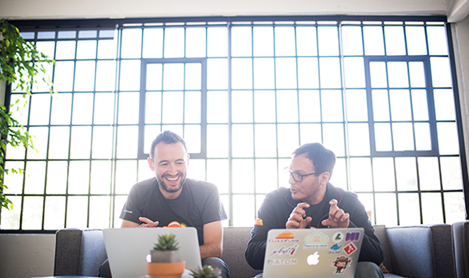 Two Cloudflare engineers collaborating on laptops in a sunlit office